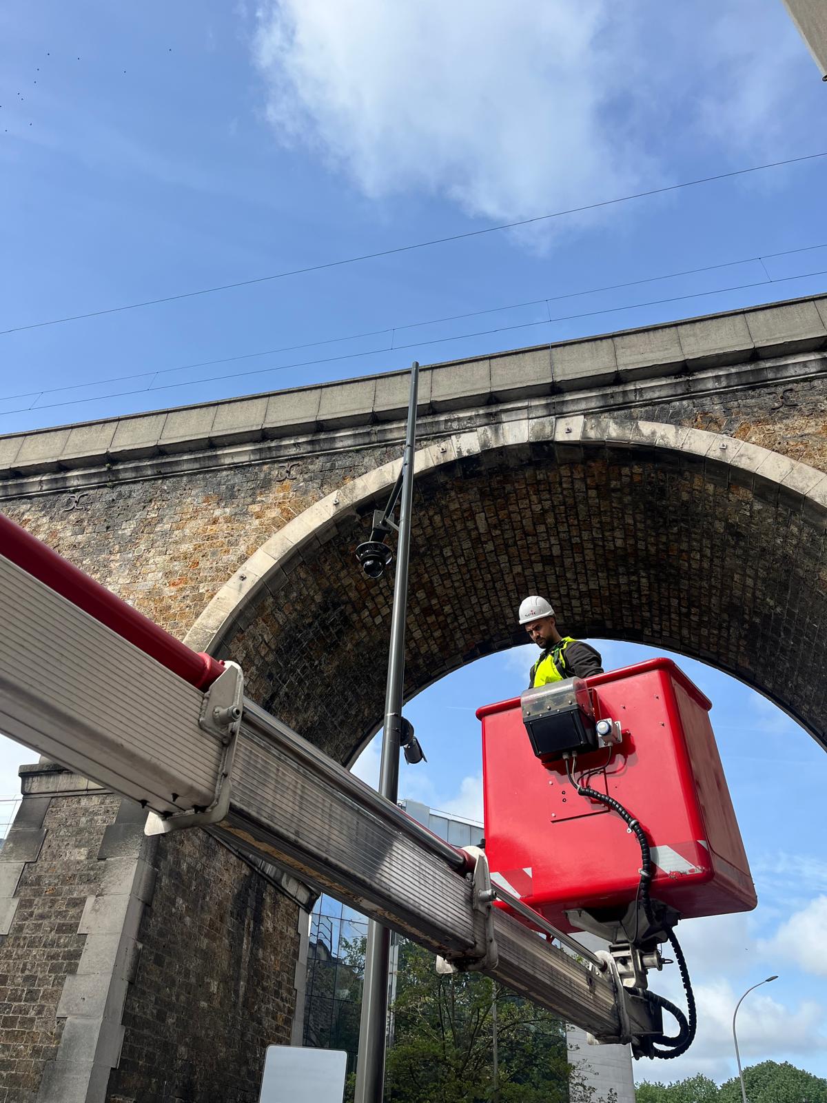 Technicien SPIE en nacelle élévatrice installant une caméra sous viaduc — Cergy